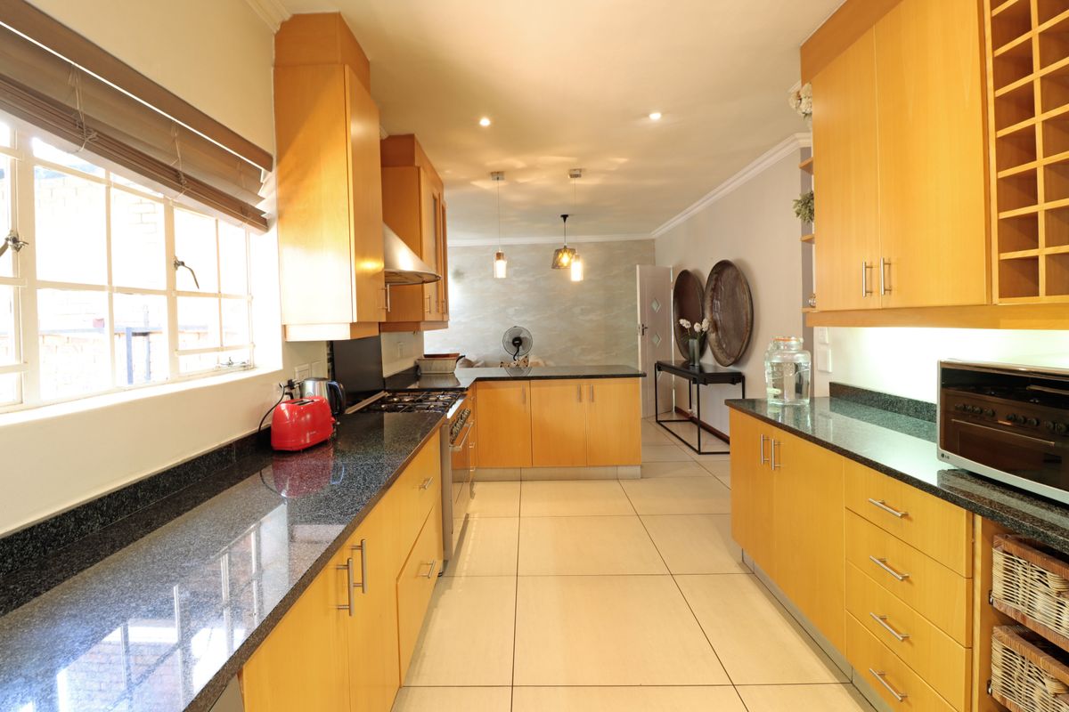 A well-maintained kitchen featuring wooden cabinetry, granite countertops, a gas hob, and an integrated oven, with tiled flooring throughout.