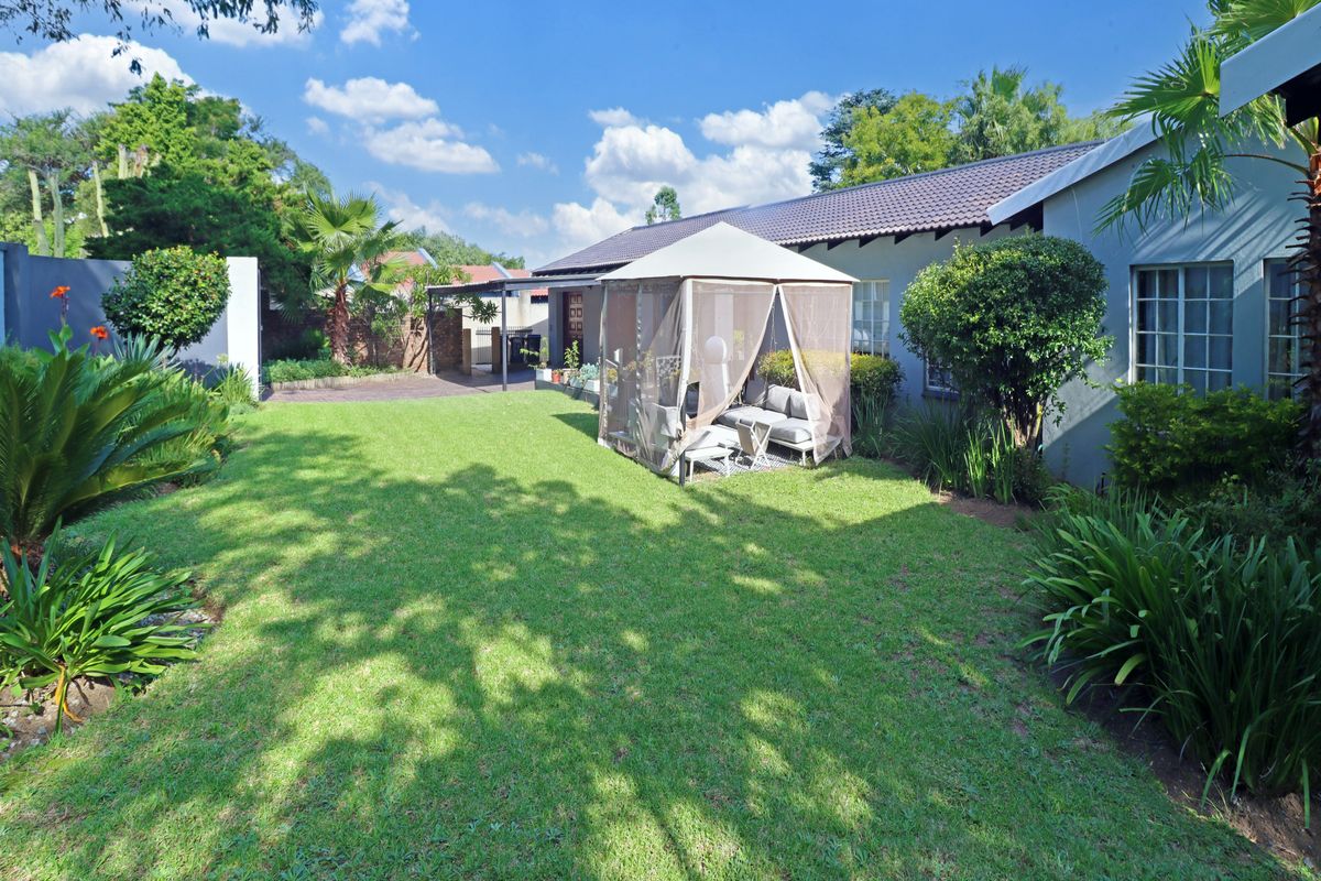 A well-maintained rear garden featuring a lush green lawn, established landscaping, and a paved area adjacent to the house.
