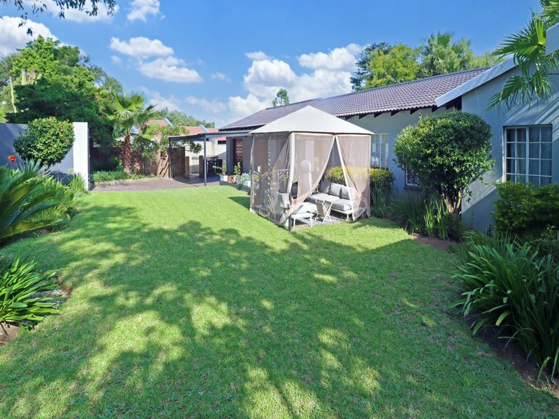 A well-maintained rear garden featuring a lush green lawn, established landscaping, and a paved area adjacent to the house.