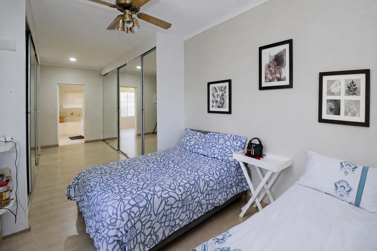 A well-maintained bedroom featuring laminate flooring, a ceiling fan, and large mirrored sliding wardrobes with direct access to an en-suite bathroom.