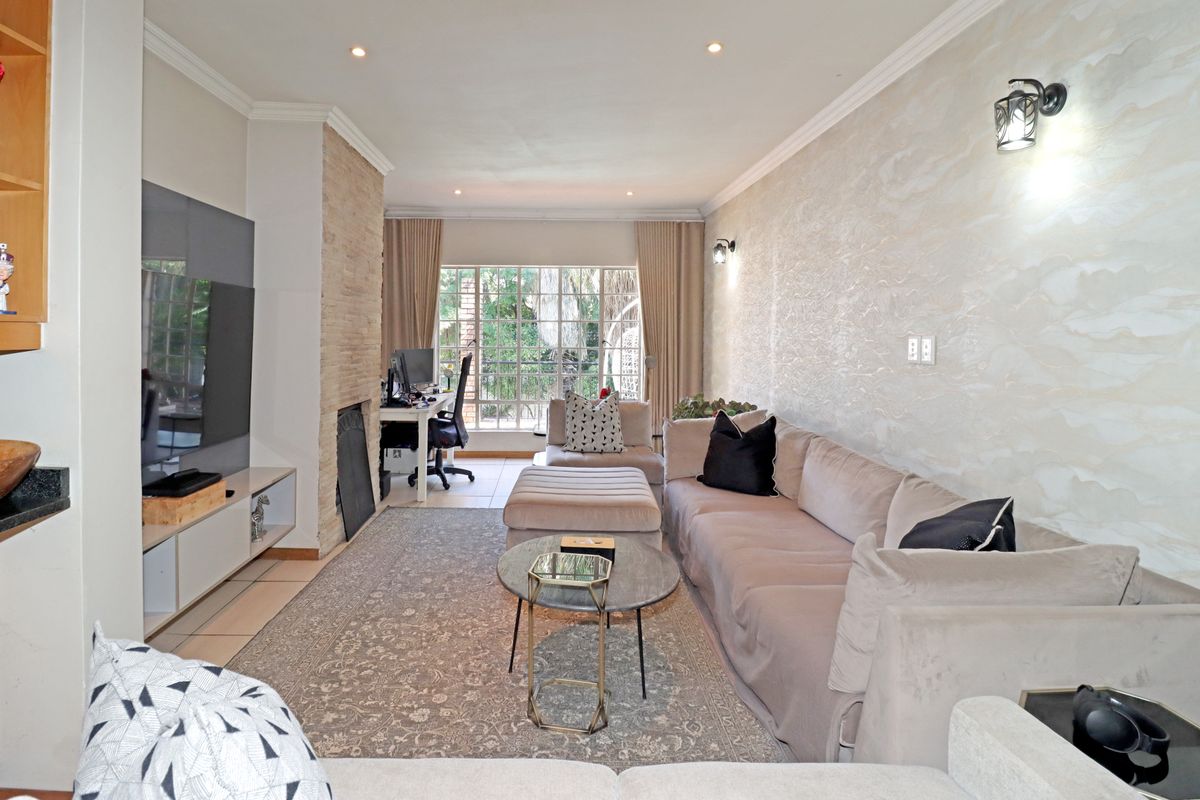 A well-maintained living room featuring a stone-clad fireplace, textured feature wall, recessed lighting, and large windows providing natural light.