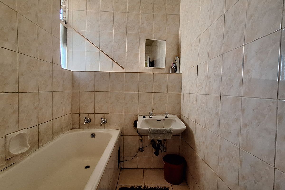 A functional bathroom featuring a bathtub and wall-mounted basin, finished with full-height ceramic wall tiling throughout.