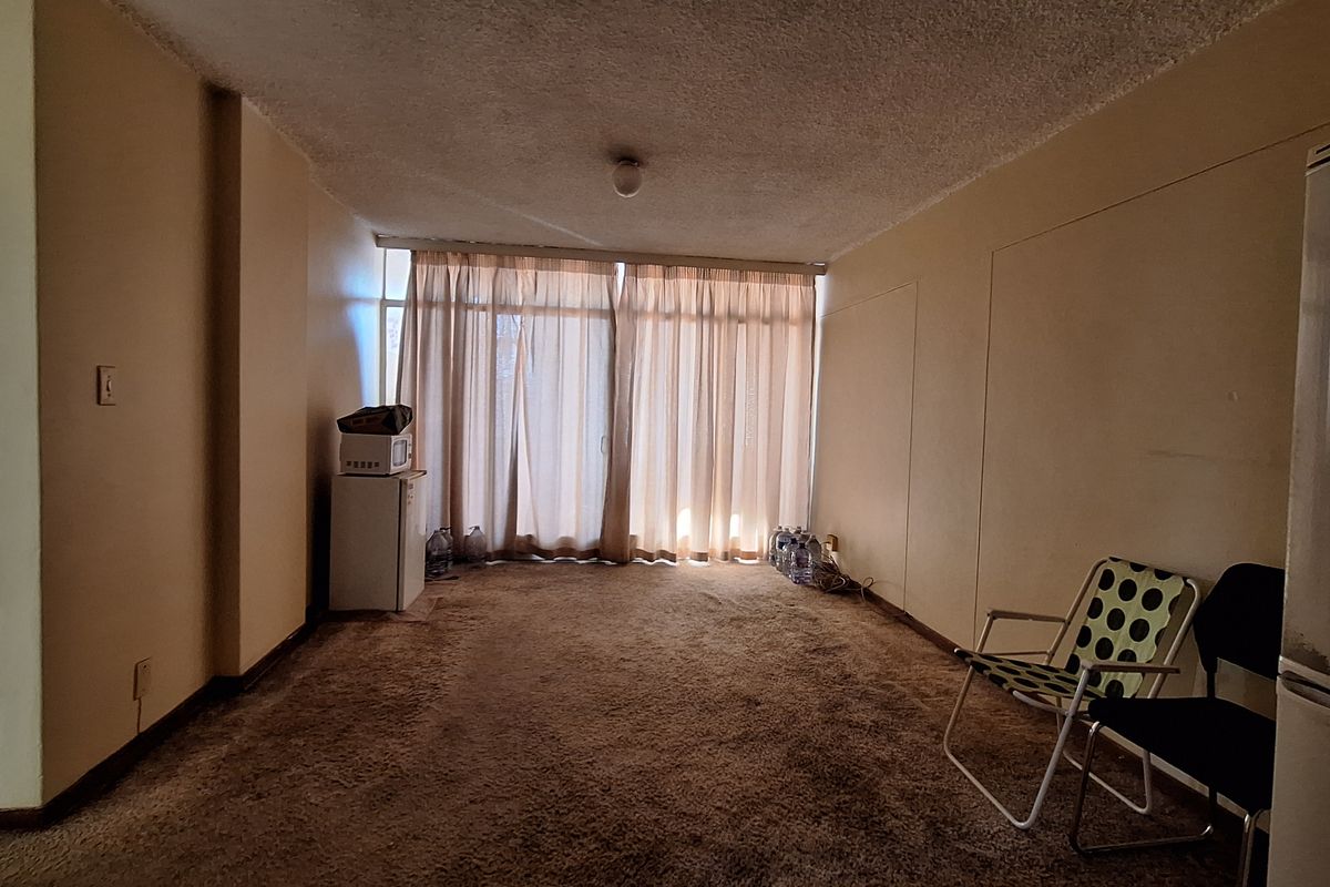 A spacious living area featuring carpeted flooring, a textured ceiling, and a large sliding glass door providing natural light.