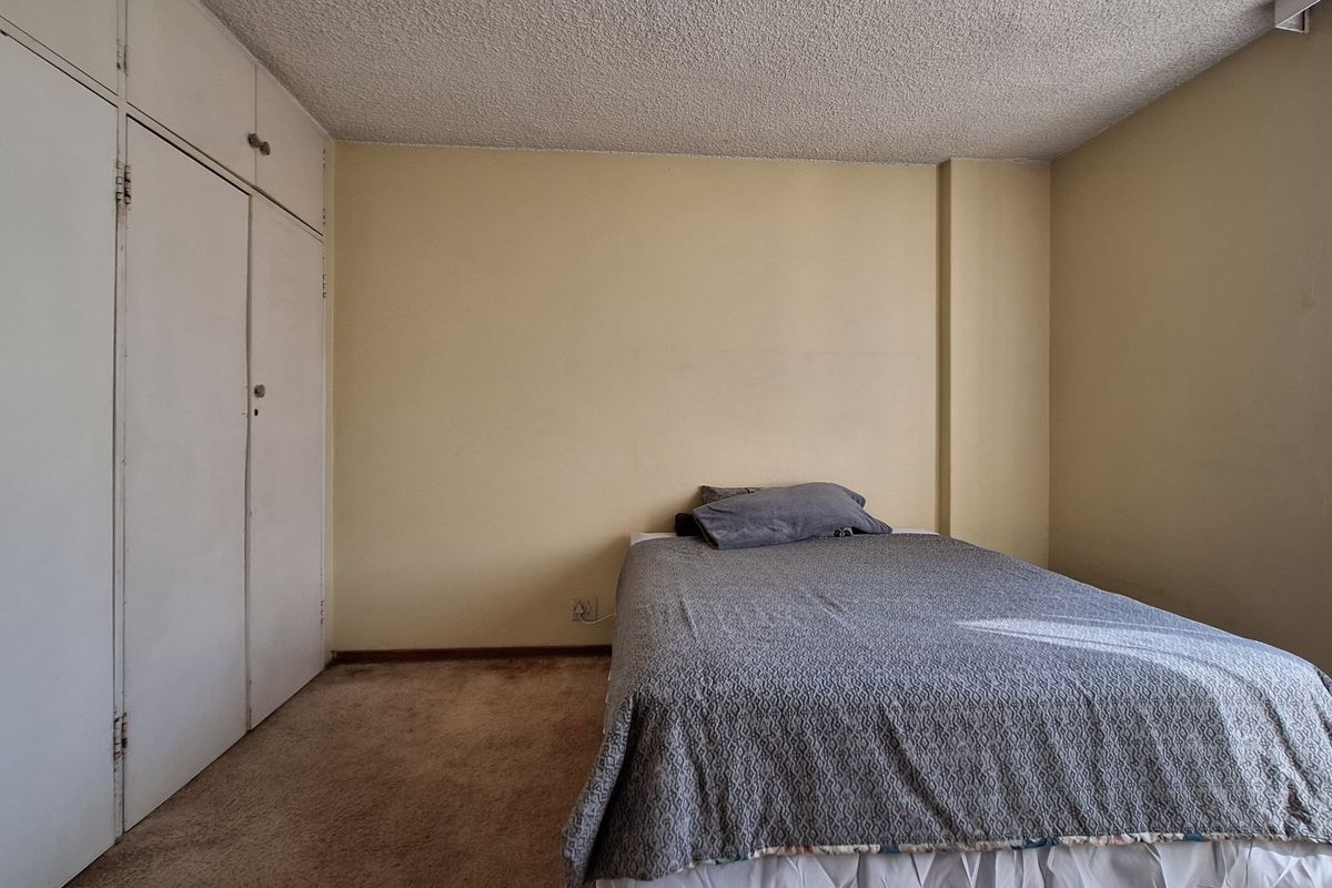 A bedroom featuring built-in cupboards, carpeted flooring, and a textured ceiling, offering a functional space with potential for cosmetic updates.