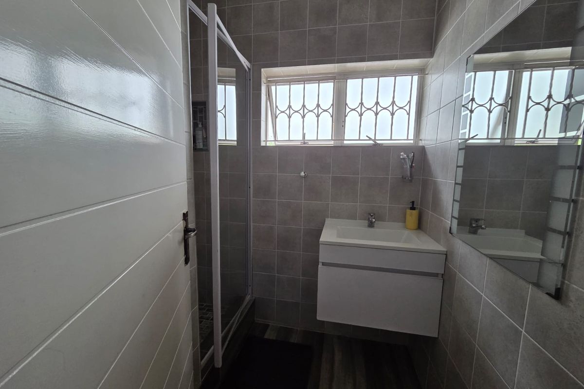 A modern, compact bathroom featuring a wall-mounted vanity, tiled walls, and a glass-enclosed shower.
