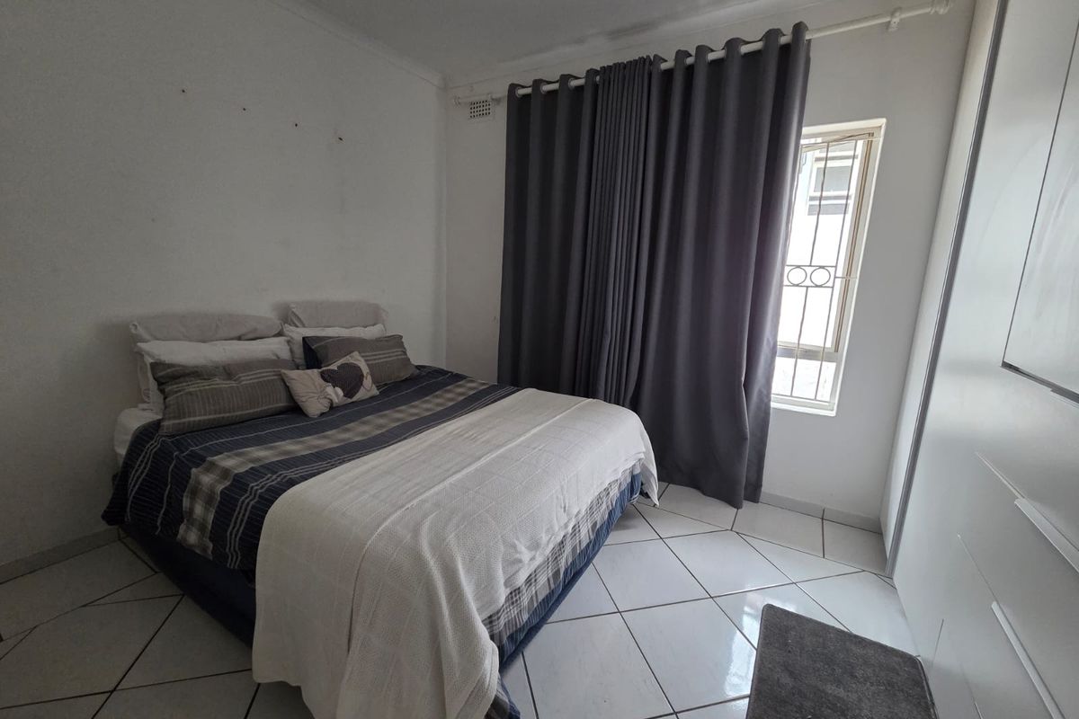 A functional bedroom featuring tiled flooring, a built-in wardrobe, and a window with security bars.