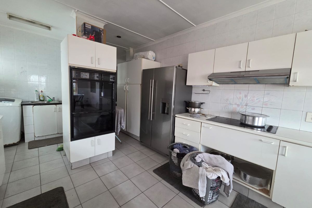 A functional kitchen featuring built-in cabinetry, a double oven, ceramic hob, extractor fan, and tiled flooring with a neutral splashback.