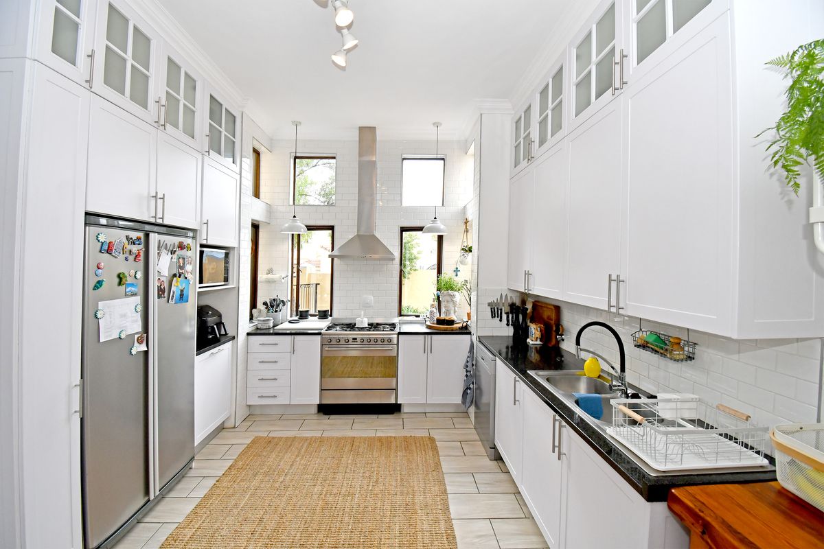 A modern galley-style kitchen featuring white cabinetry, black granite countertops, stainless steel appliances, and subway tile backsplash with ample natural light.