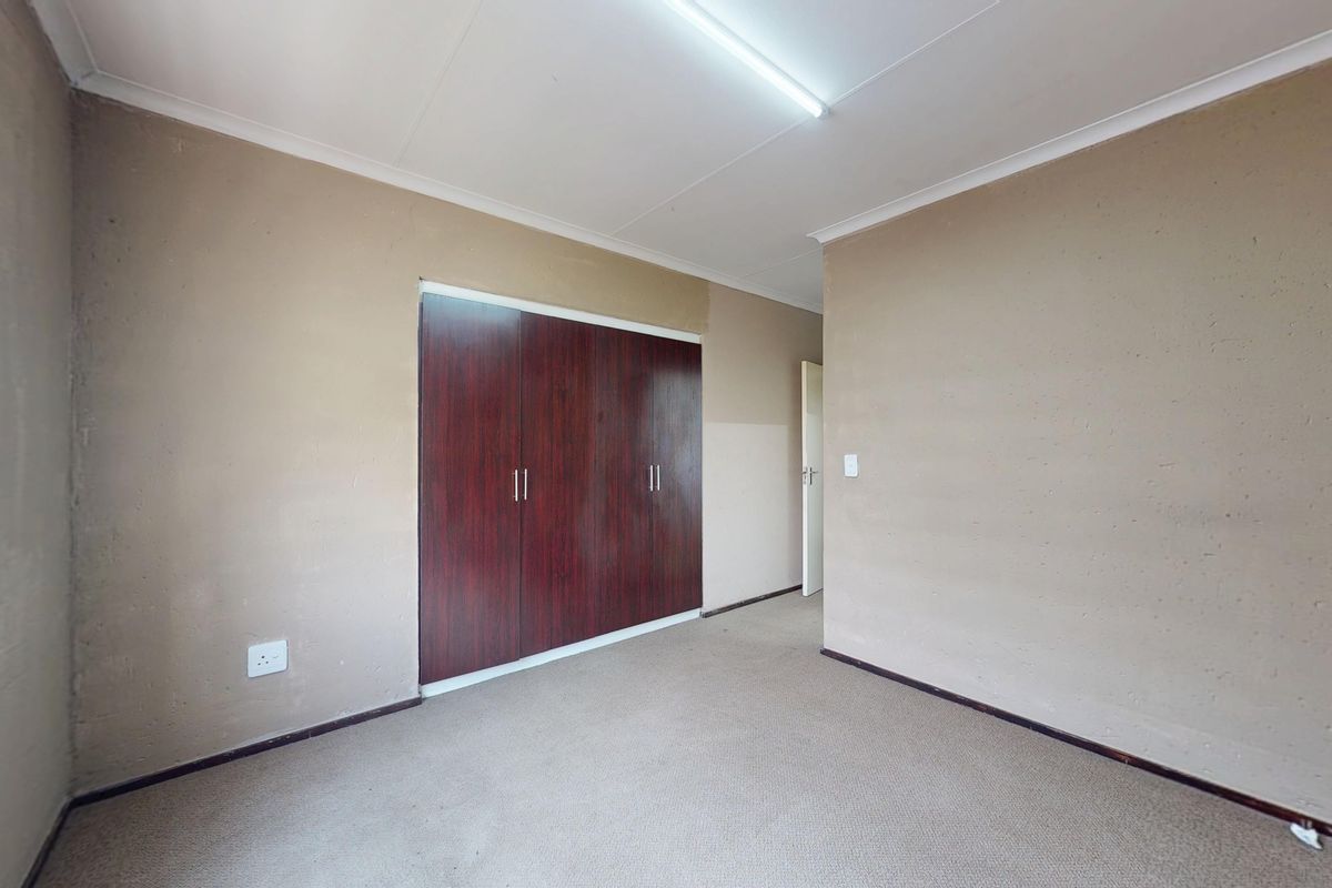 A vacant bedroom featuring built-in wooden cupboards, carpeted flooring, and neutral wall tones, offering a blank canvas for personalization.