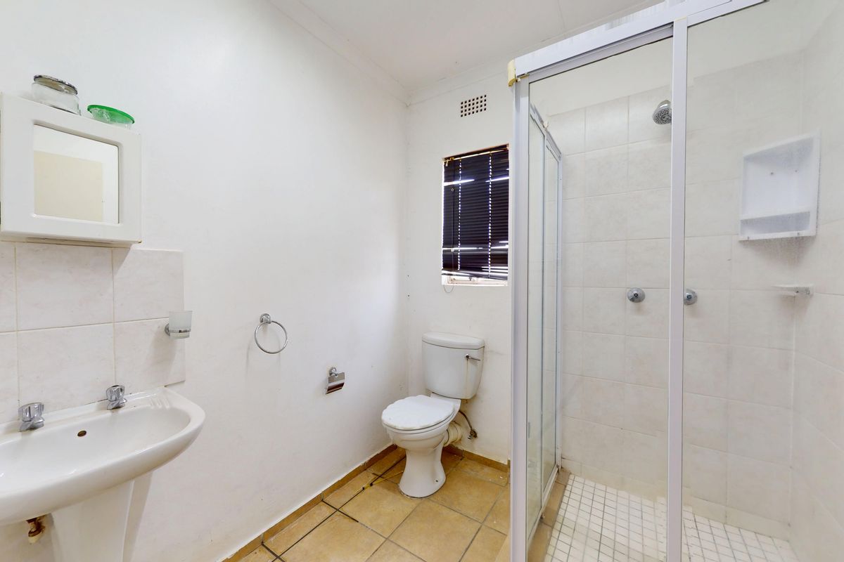 A functional bathroom featuring a pedestal basin, toilet, and a glass-enclosed shower with tiled walls and flooring.