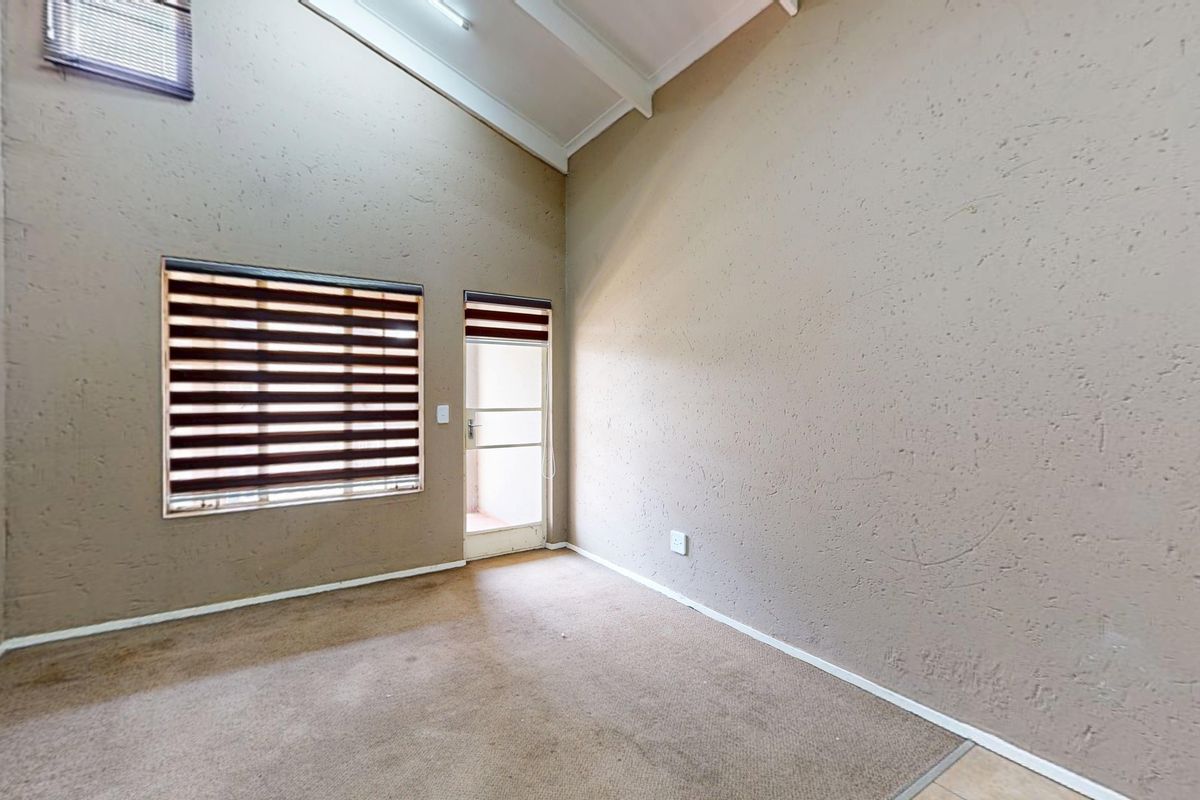 An empty living room featuring high vaulted ceilings, carpeted flooring, and natural light through a window with fitted roller blinds.