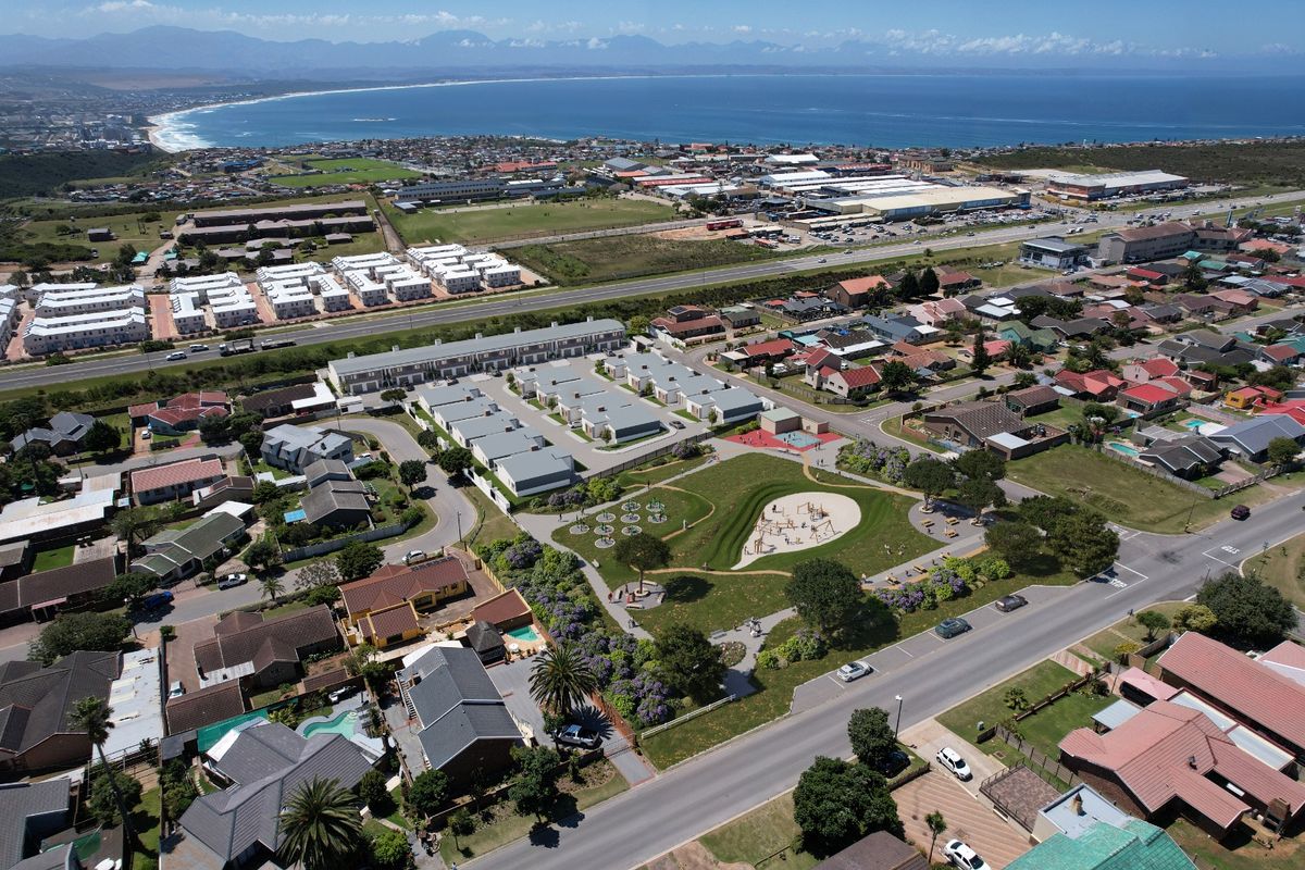 Aerial view of a residential estate featuring a central park, playground, and surrounding housing units with coastal and mountain views in the distance.