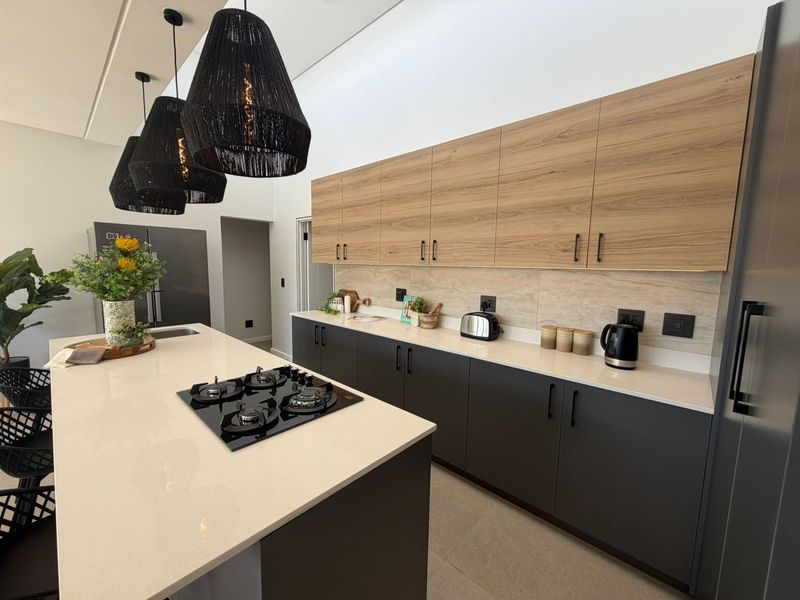 Modern kitchen featuring a large central island with a built-in gas hob, sleek two-tone cabinetry, stone countertops, and contemporary pendant lighting.