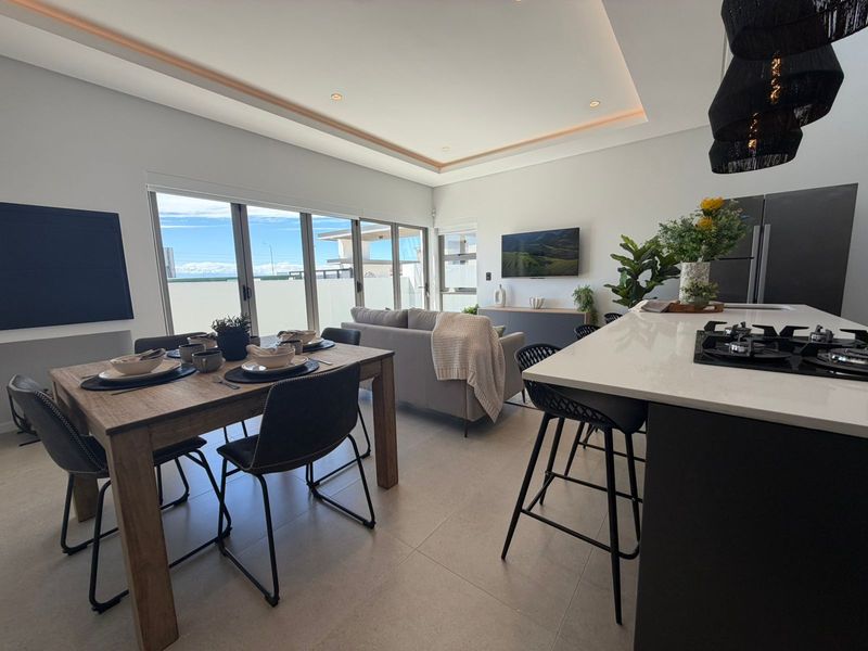 Modern open-plan living area featuring a sleek kitchen with a central island, gas hob, and seamless flow to the outdoor patio through sliding doors.