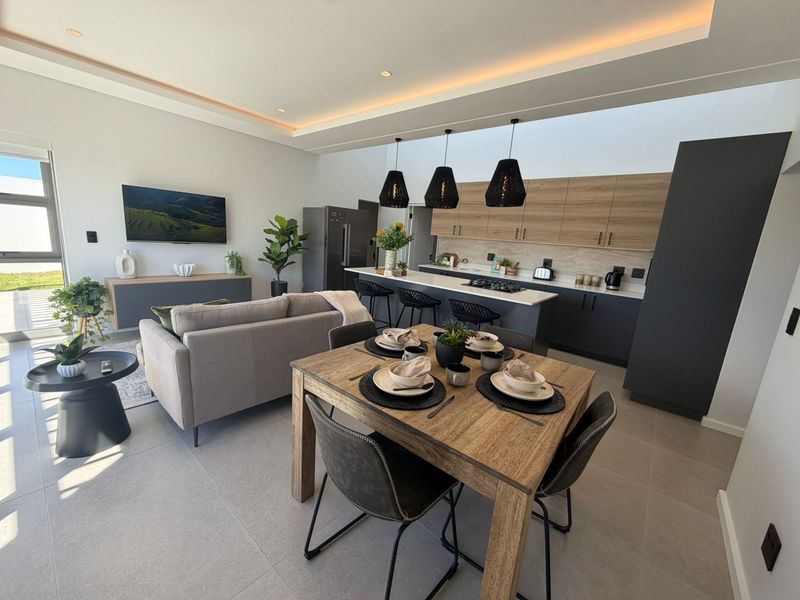 Modern open-plan living area featuring a sleek kitchen with breakfast bar, dining space, and lounge, all finished with contemporary cabinetry and recessed ceiling lighting.