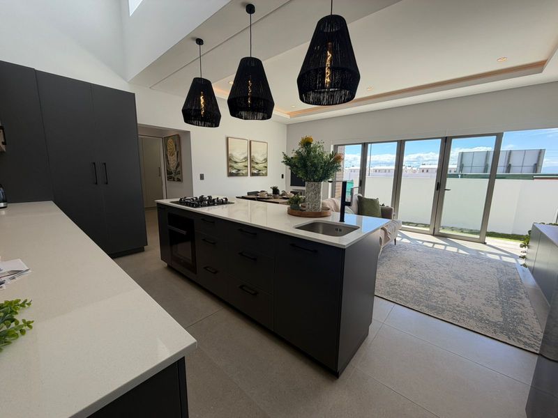 Modern open-plan kitchen and living area featuring a large central island with integrated hob, sleek cabinetry, and sliding doors leading to a balcony.