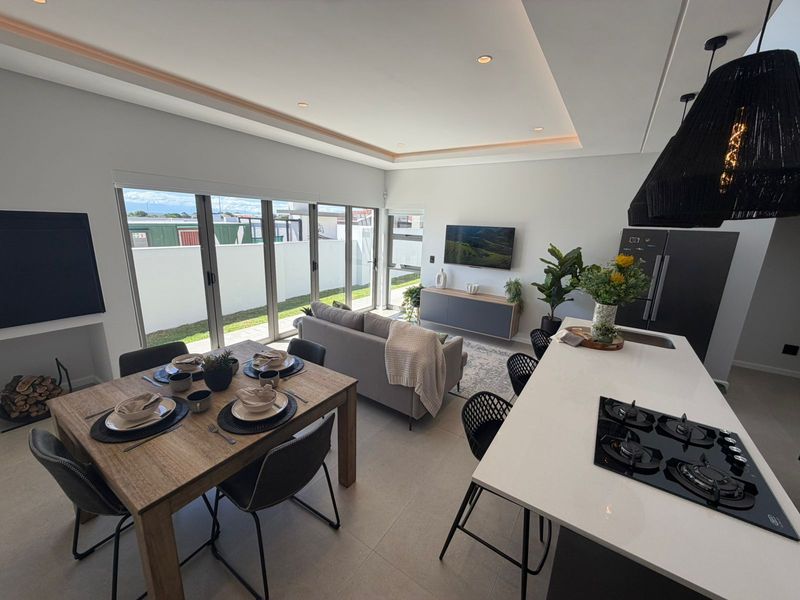 Modern open-plan living area featuring a sleek kitchen with a central island, gas hob, and seamless flow to the outdoor patio through sliding doors.