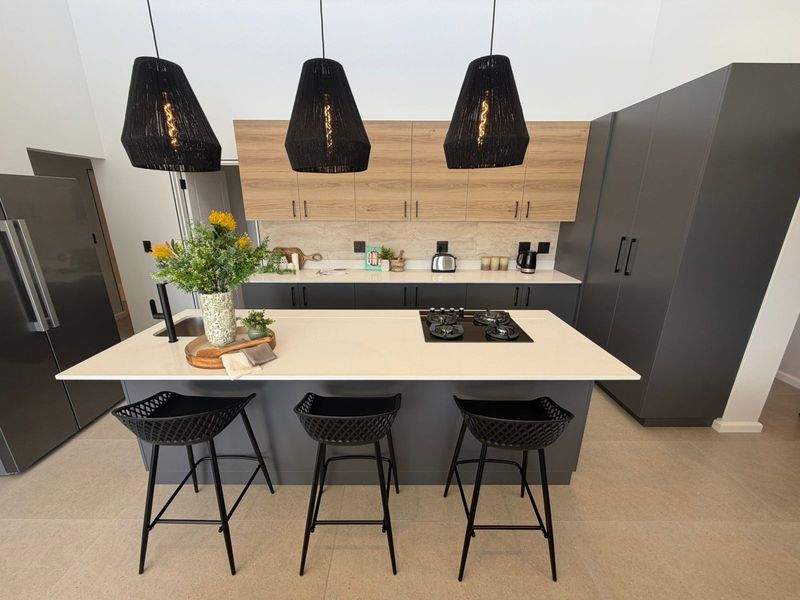 Modern kitchen featuring a central island with a built-in gas hob, stone countertops, two-tone cabinetry, and contemporary pendant lighting.