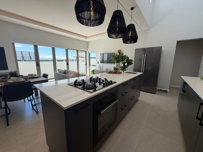 Modern open-plan kitchen featuring a large central island with a built-in gas hob, oven, and stone countertops, seamlessly flowing into the living and dining area.