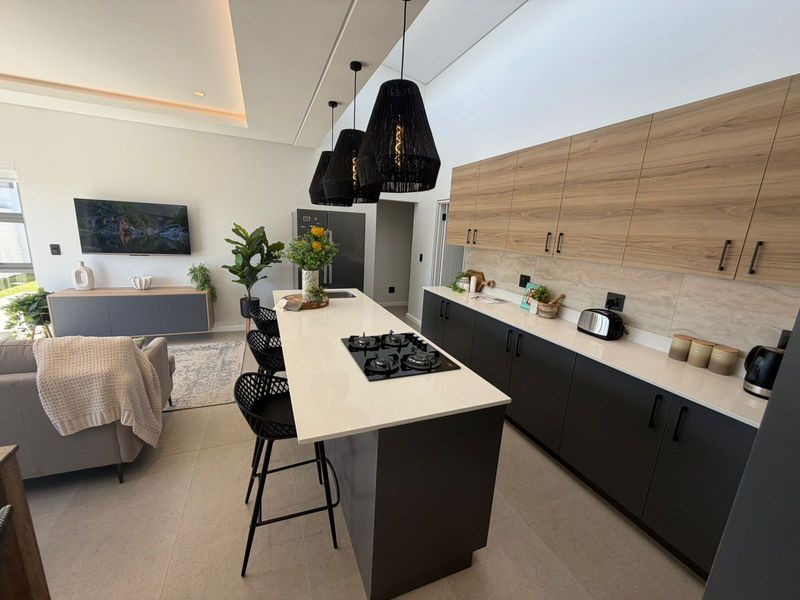 Modern open-plan kitchen featuring a central island with a built-in gas hob, stone countertops, and sleek two-tone cabinetry, seamlessly flowing into the living area.