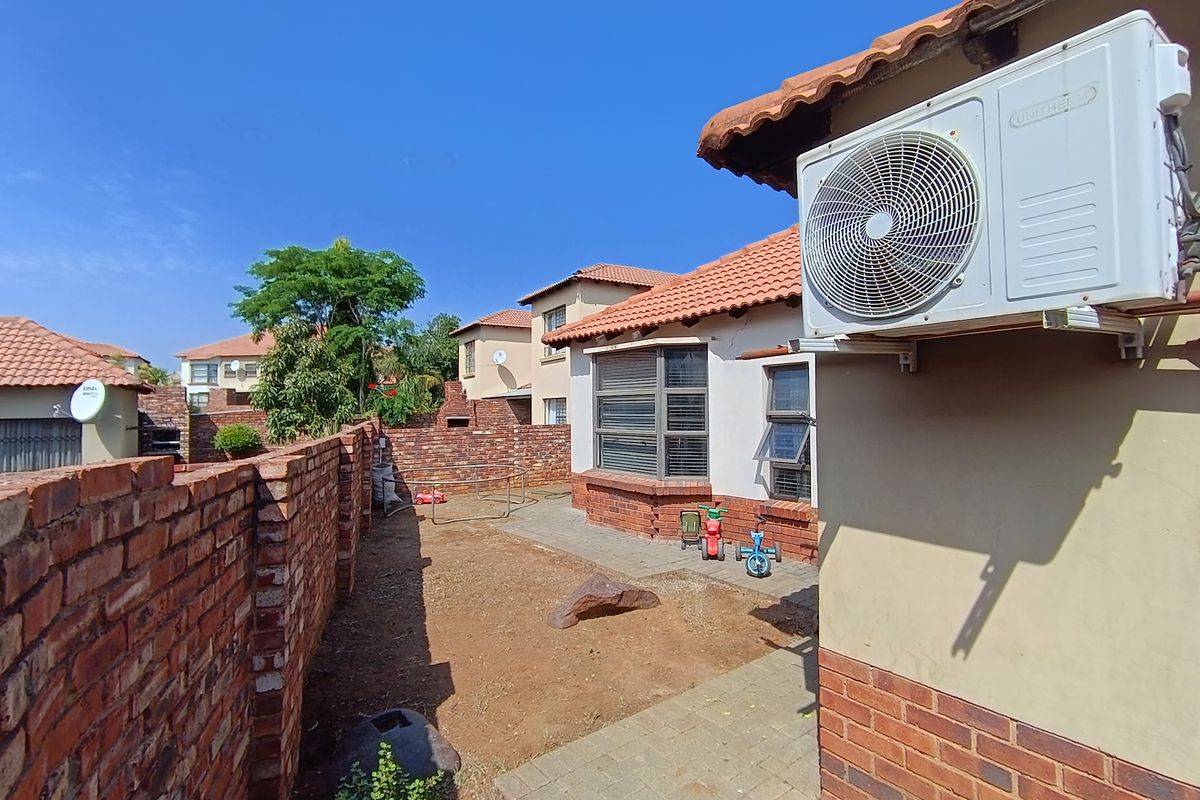 Rear exterior view of the townhouse featuring a brick boundary wall, paved walkway, and an installed air conditioning unit.