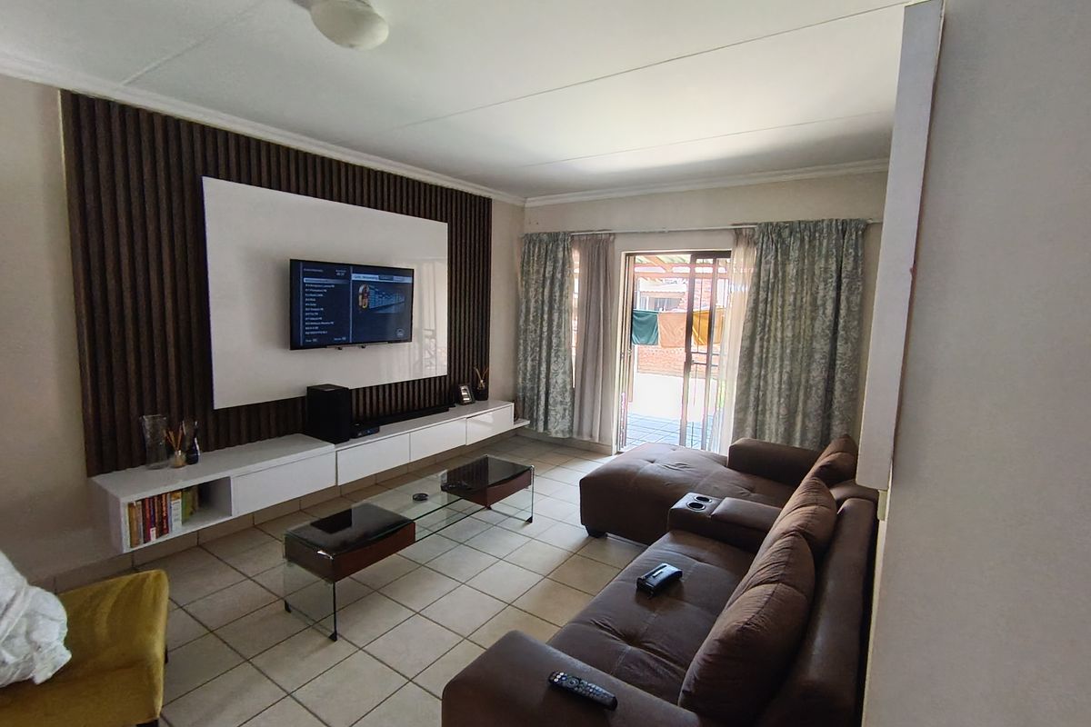 A comfortable living room featuring a modern built-in media wall with slatted timber accents, tiled flooring, and direct access to an outdoor patio area.