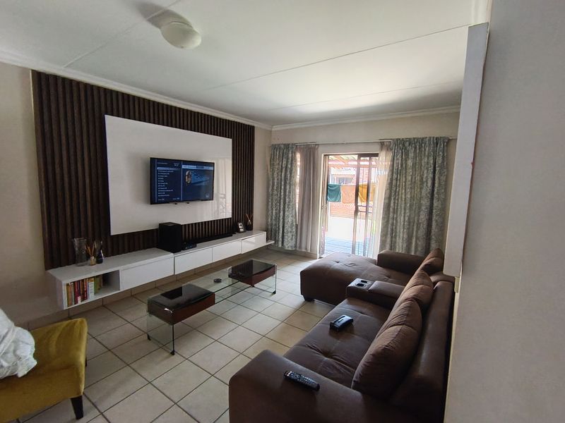 A comfortable living room featuring a modern built-in media wall with slatted timber accents, tiled flooring, and direct access to an outdoor patio area.