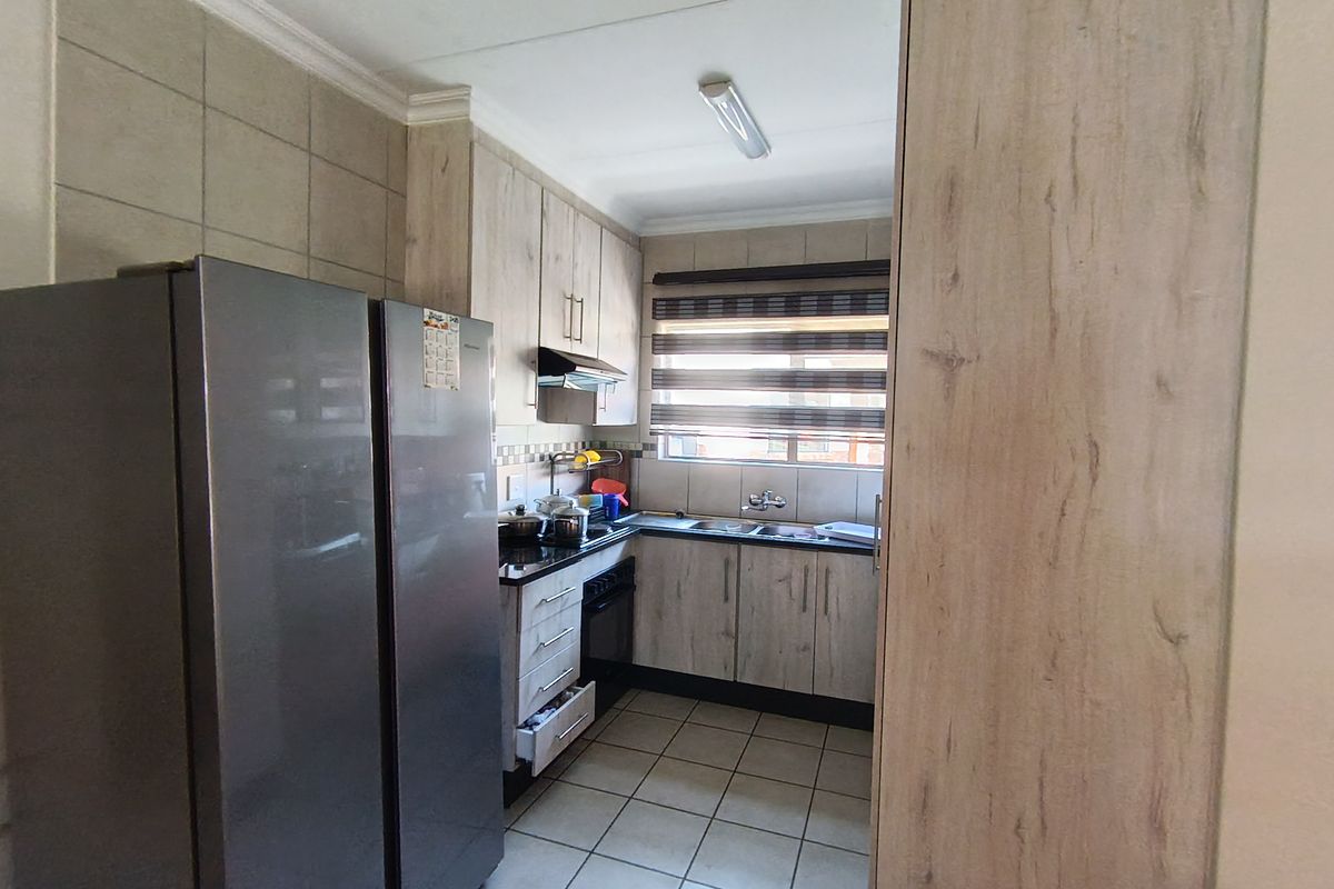 A functional kitchen featuring light wood-look cabinetry, dark countertops, tiled flooring, and a double basin sink with a window view.