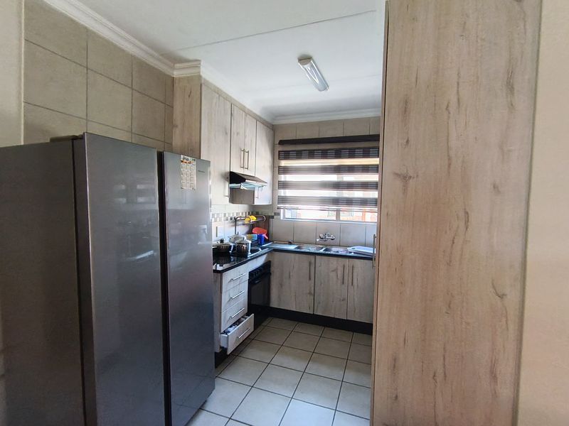 A functional kitchen featuring light wood-look cabinetry, dark countertops, tiled flooring, and a double basin sink with a window view.