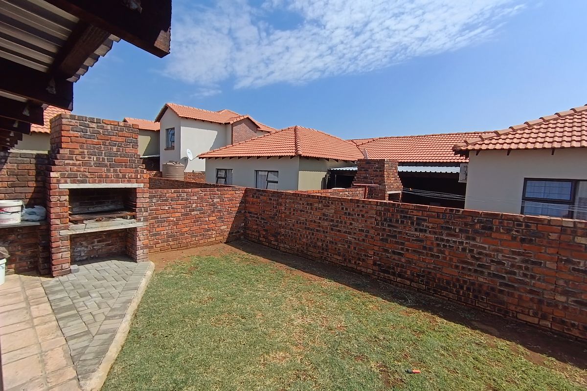 A private rear garden featuring a built-in brick braai, paved patio area, and established lawn, enclosed by a sturdy brick boundary wall.