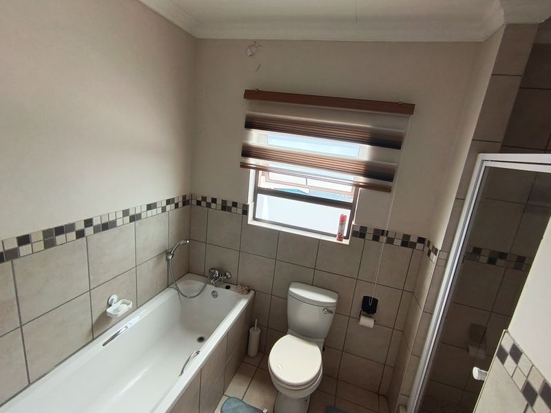 A functional bathroom featuring a bathtub, separate shower enclosure, and toilet with neutral wall tiling and a window for natural light.
