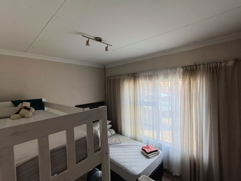 A functional bedroom featuring tiled flooring, track lighting, and large windows with curtain treatments, providing natural light to the space.