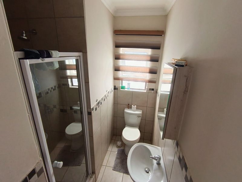 Compact bathroom featuring a shower enclosure, toilet, and pedestal basin with neutral wall and floor tiling.