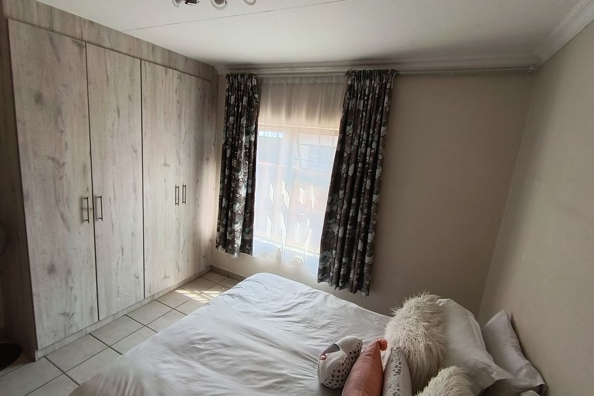 A bedroom featuring built-in cupboards with a wood-look finish, tiled flooring, and a window with curtain treatments.