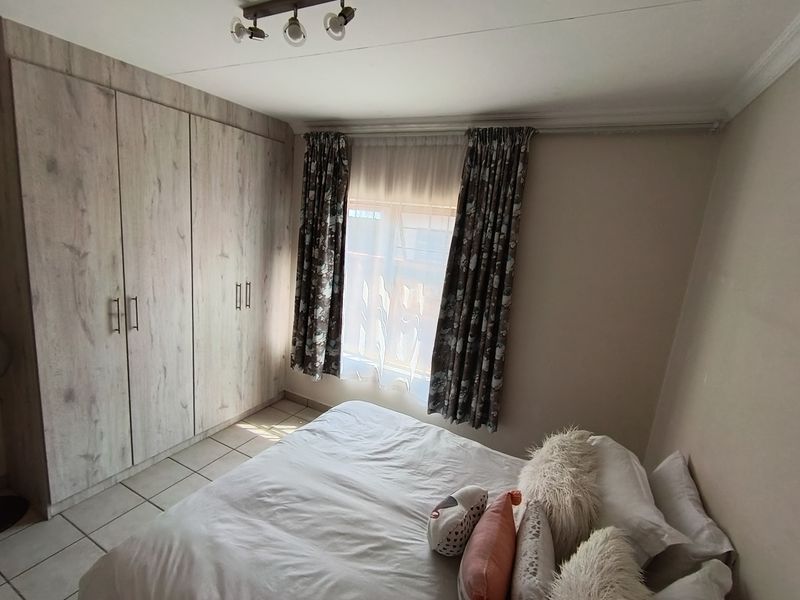A bedroom featuring built-in cupboards with a wood-look finish, tiled flooring, and a window with curtain treatments.