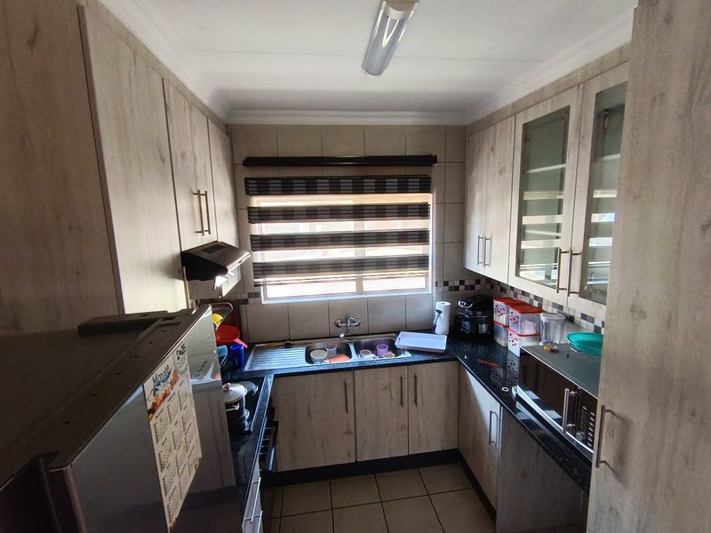 A compact kitchen featuring laminate cabinetry, granite countertops, a double basin sink, and a tiled backsplash, offering functional storage and workspace.