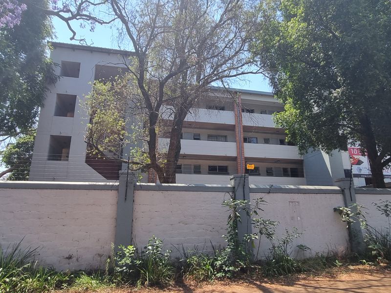 Exterior view of a multi-story apartment building featuring a perimeter wall with electric fencing and mature trees.