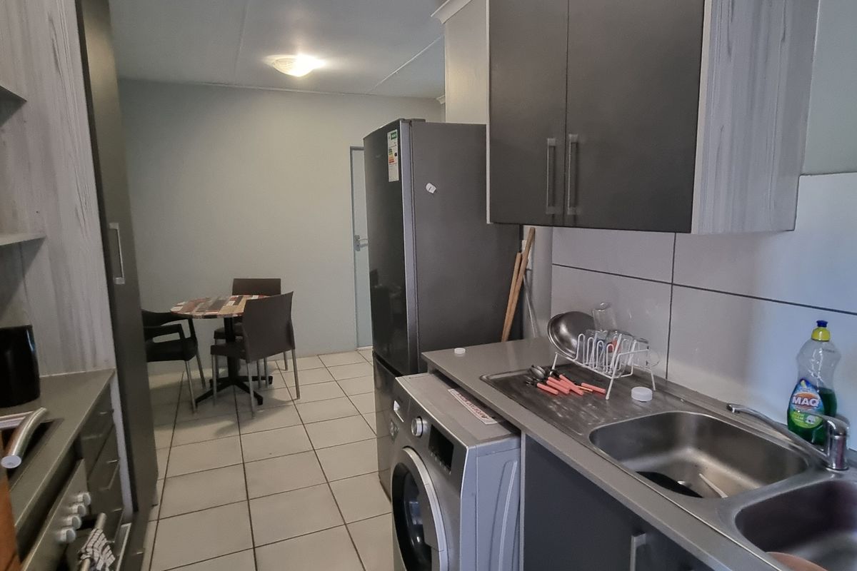 A functional kitchen area featuring built-in cabinetry, a double bowl stainless steel sink, and tiled flooring, providing a practical workspace.