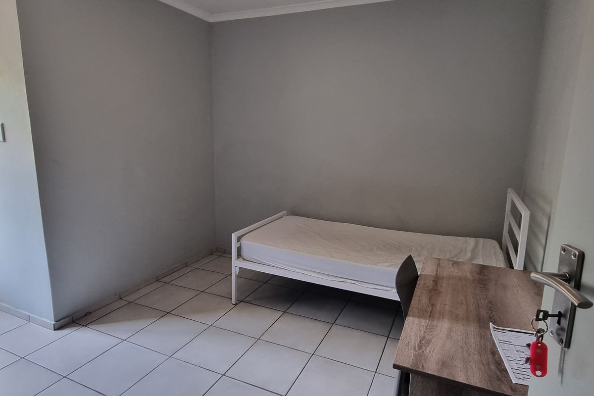 A simple bedroom featuring tiled flooring and neutral wall finishes, providing a functional space for a single bed and study area.