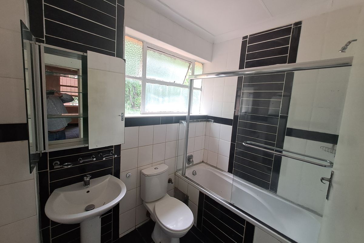 A functional bathroom featuring a pedestal basin, toilet, and a bathtub with a glass shower screen, finished with black and white wall tiling.
