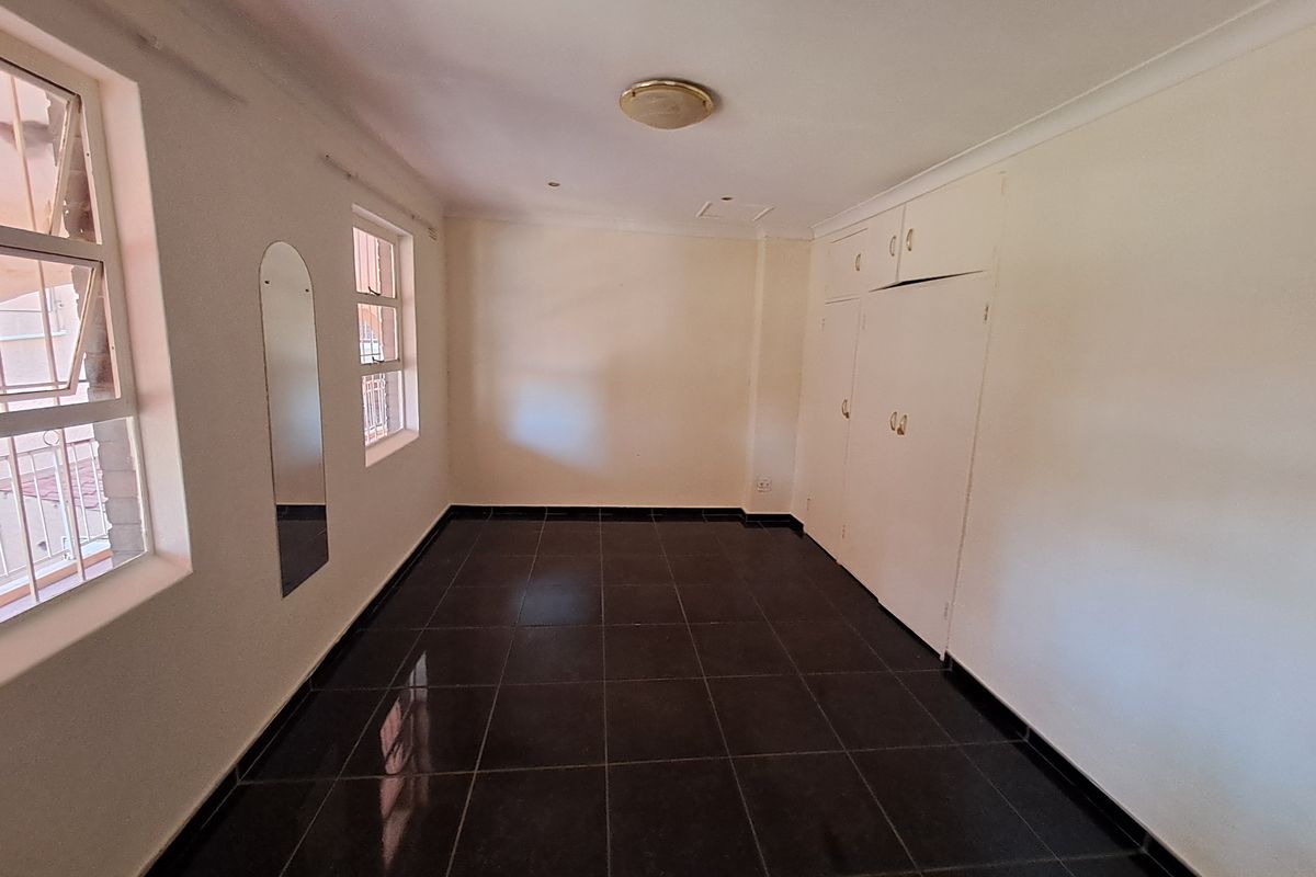 A bright, empty bedroom featuring dark tiled flooring, built-in white cabinetry, and large windows allowing for natural light.