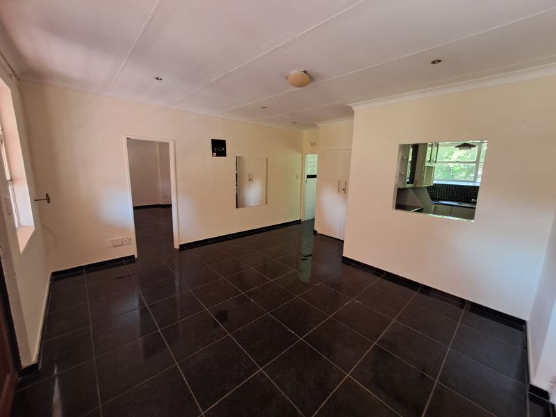 An open-plan living area featuring dark tiled flooring, a serving hatch to the kitchen, and access to adjacent rooms.