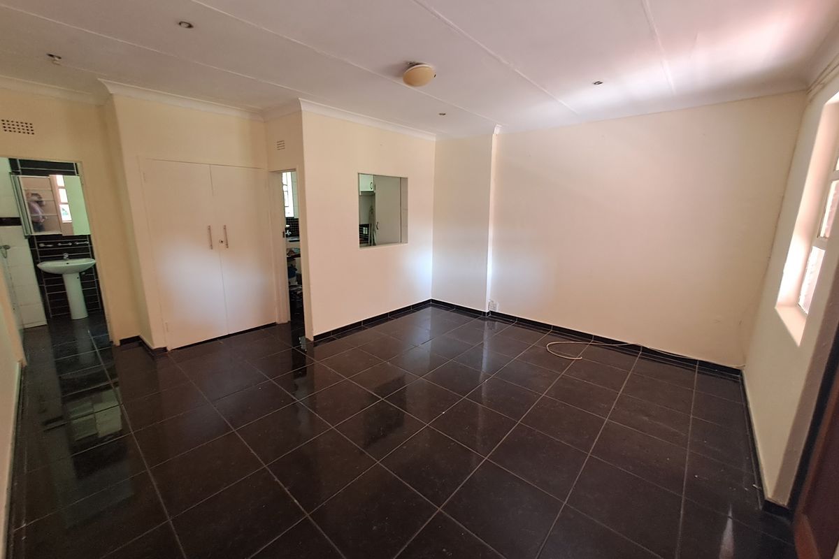 An empty living area featuring dark tiled flooring, built-in storage cupboards, and a view into the adjacent kitchen area.