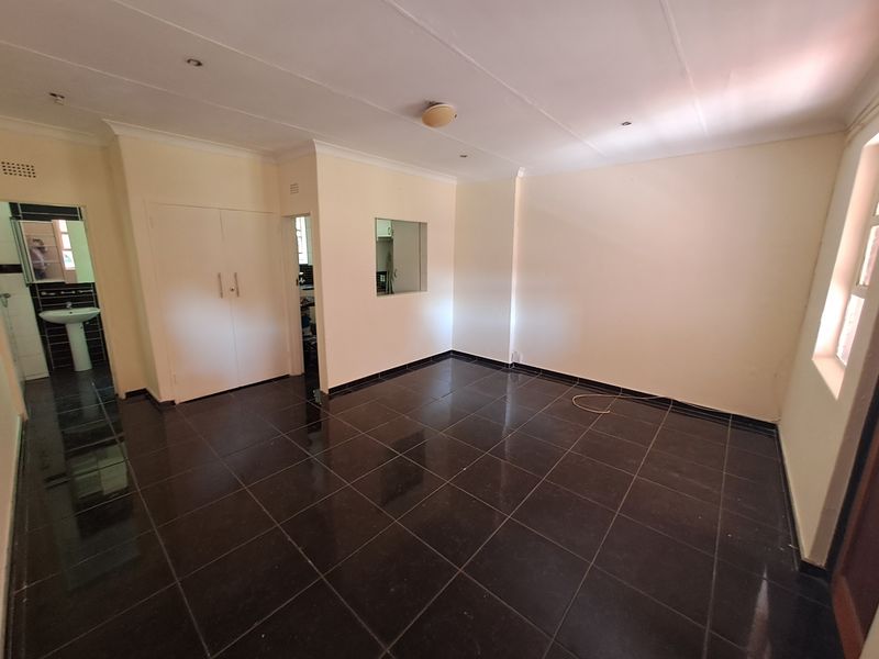 An empty living area featuring dark tiled flooring, built-in storage cupboards, and a view into the adjacent kitchen area.