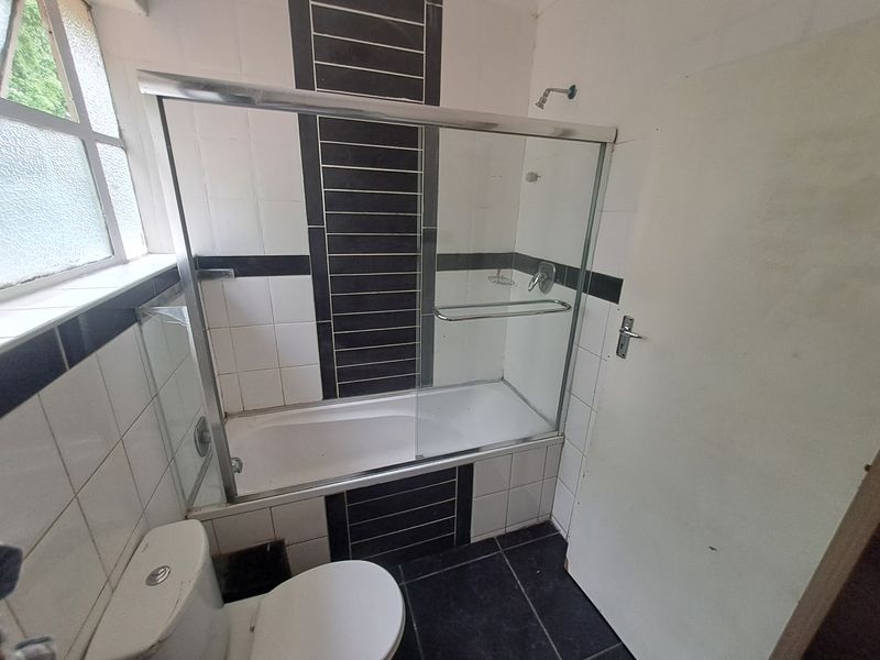 A functional bathroom featuring a bathtub with a glass shower screen, tiled walls with decorative accents, and a standard toilet.