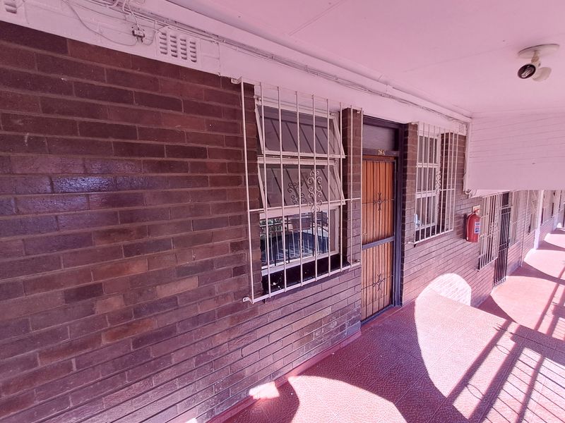 Exterior view of an apartment entrance featuring a brick facade, security gate, and protective window bars.
