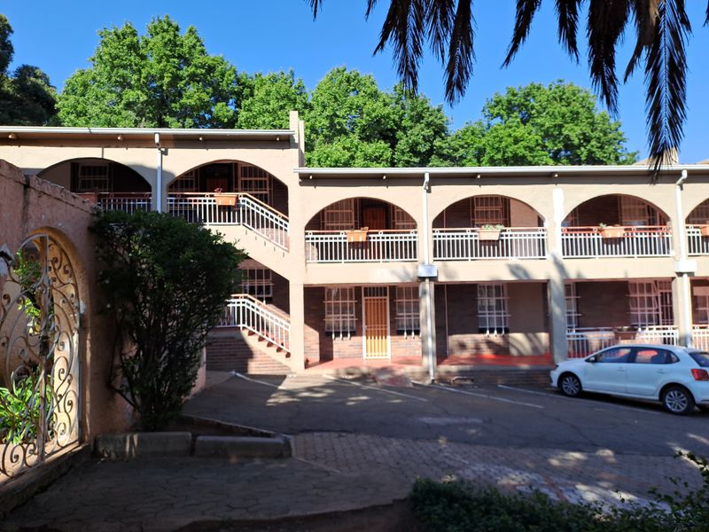 Exterior view of a multi-story apartment complex featuring arched balconies, brickwork detailing, and an open-air staircase leading to upper-level units.