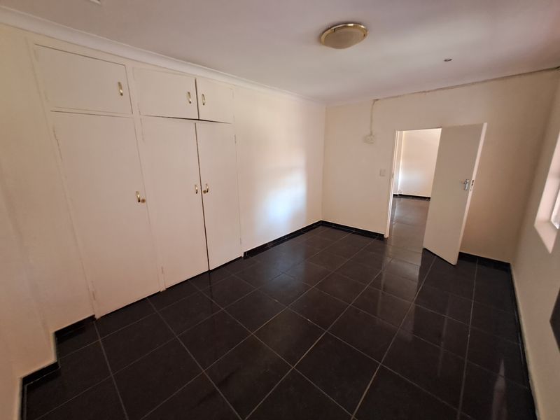 A vacant bedroom featuring dark tiled flooring and built-in white cabinetry, offering a clean and functional space ready for personalization.