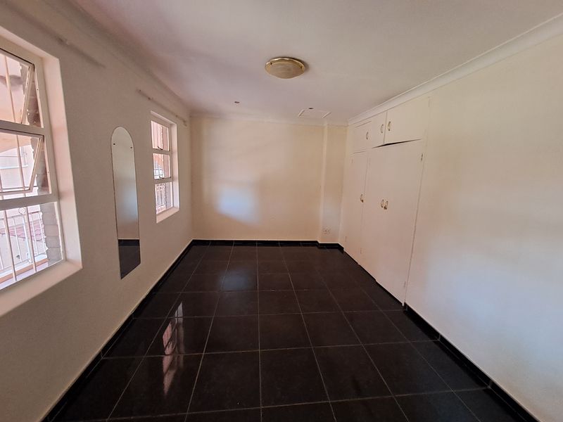 A bright, empty bedroom featuring dark tiled flooring, built-in white cabinetry, and large windows allowing for natural light.