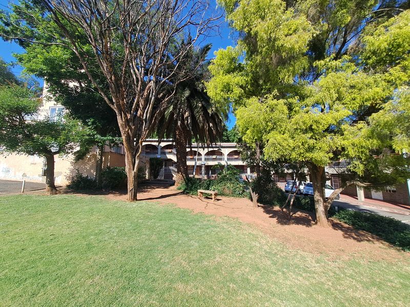 A view of the apartment complex exterior featuring landscaped garden areas, mature trees, and multi-level balcony walkways.